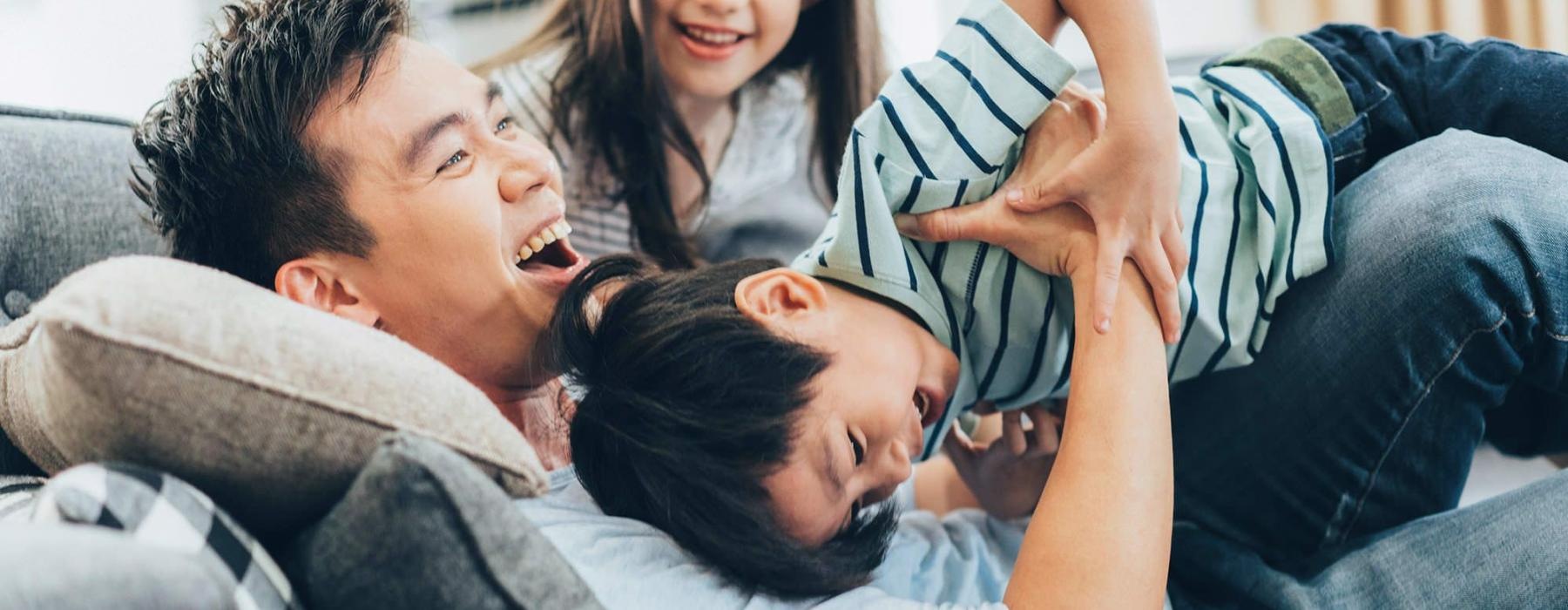 father plays on a couch with his young children